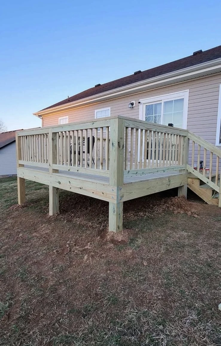 Raised wood deck with railing beside a home