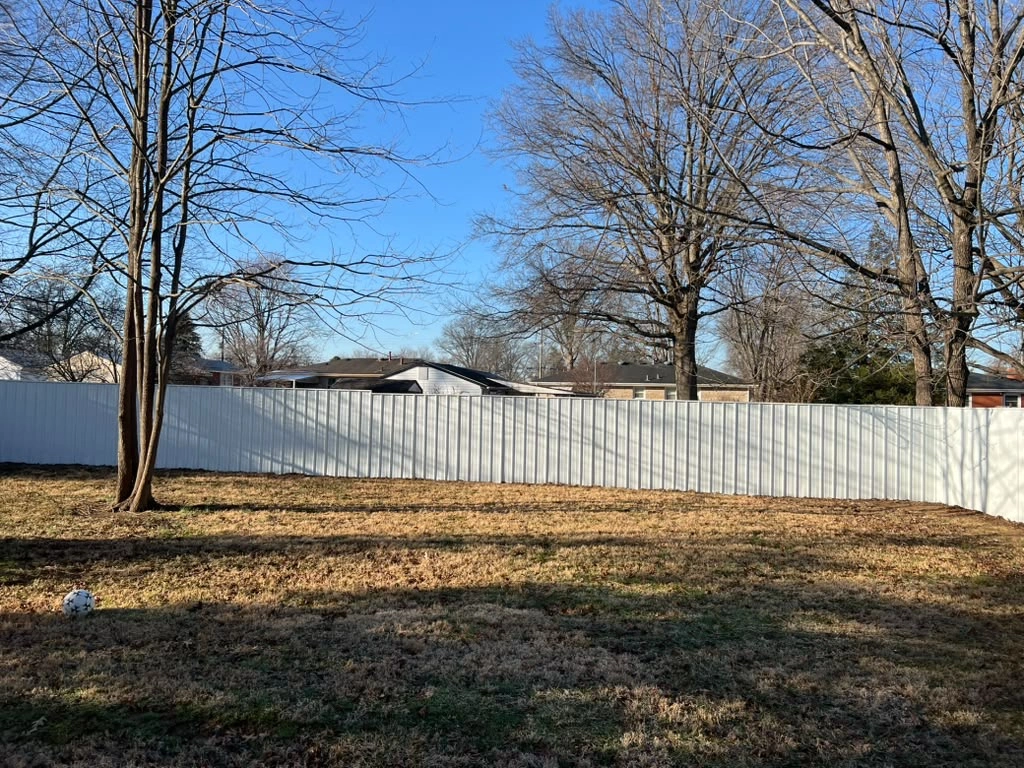 White privacy fence along a tree-lined backyard